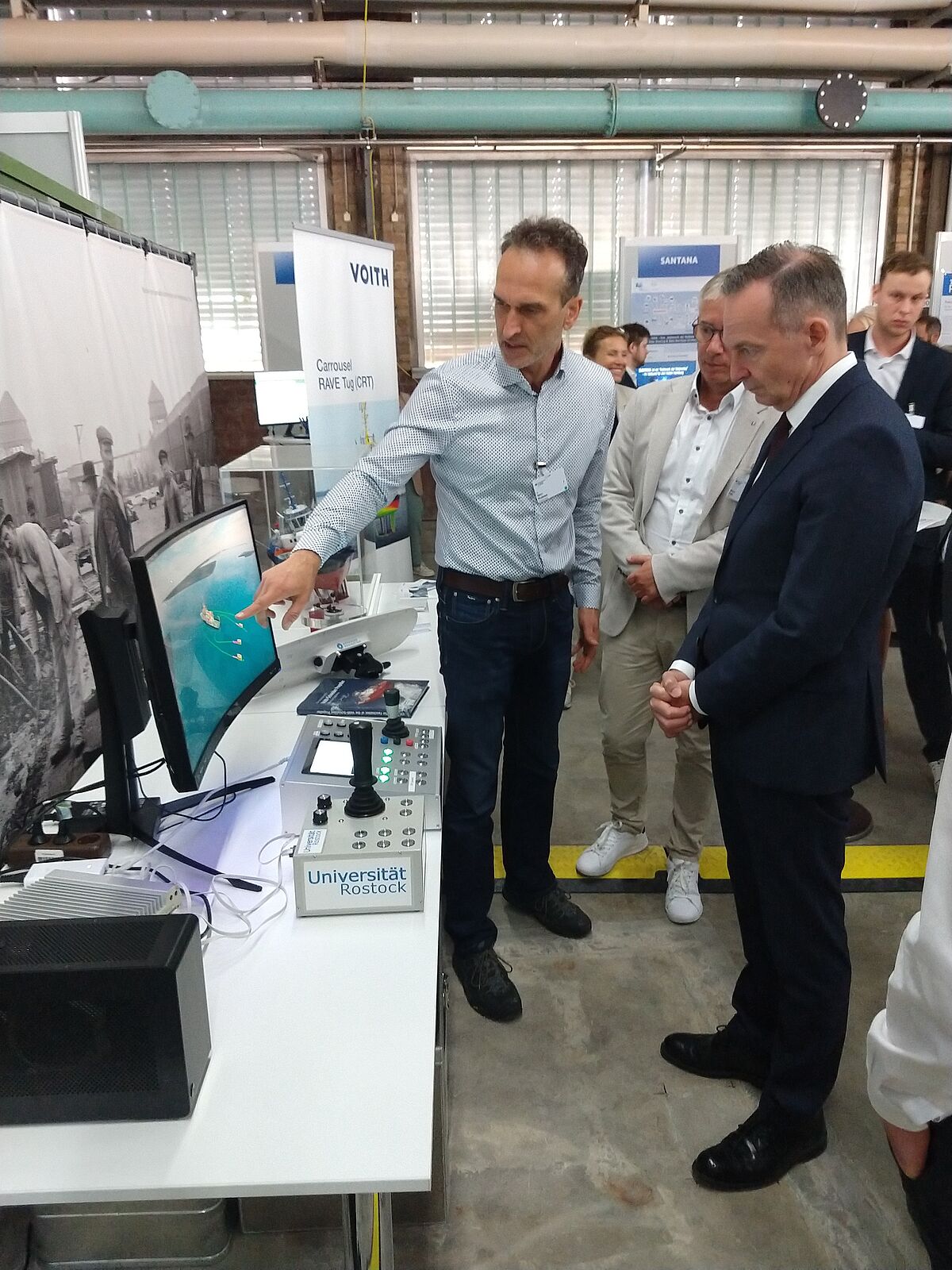 Dr.-Ing. Björn Kolewe demonstriert dem Bundesminister für Digitales und Verkehr, Dr. Volker Wissing, die Funktionalitäten einer mobilen Kommandozentrale für den kooperativen Betrieb autonomer, elektrisch angetriebener Schub- und Schleppermodule zur Schiffsassistenz (Foto: Torsten Jeinsch/Universität Rostock).